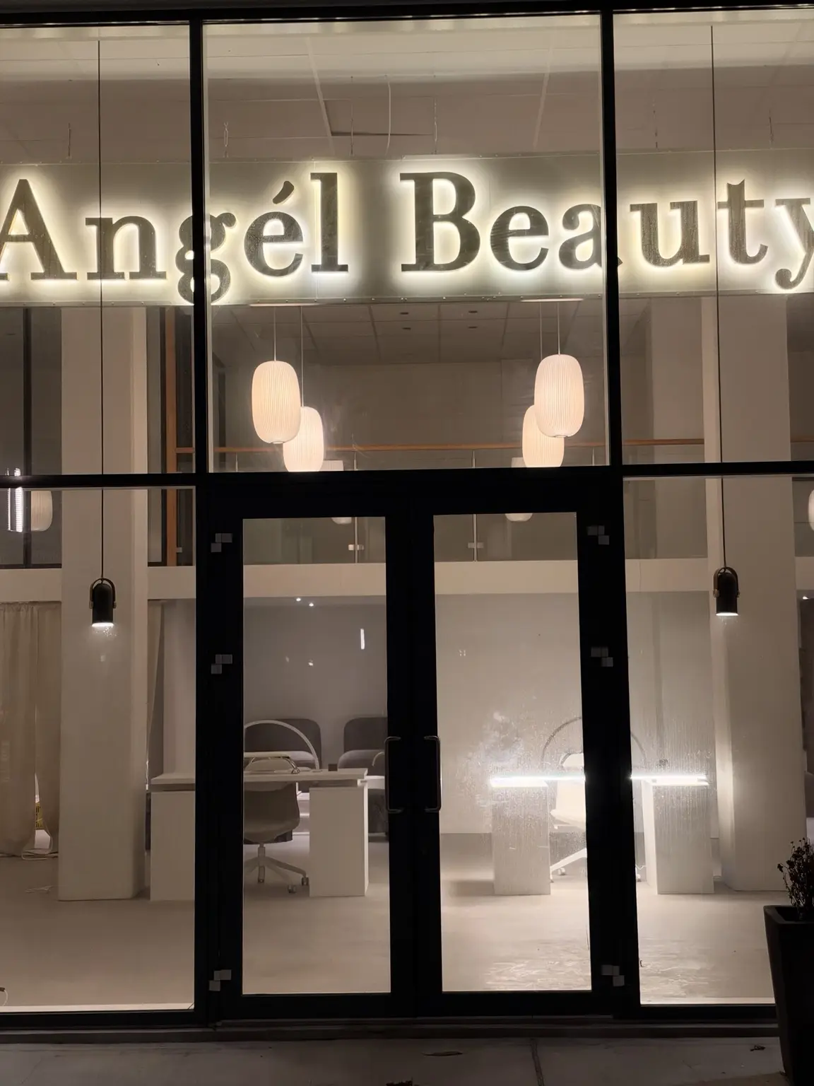 Loftophængt, bagbelyst Angel Beauty-skilt set gennem salonens glasfacade